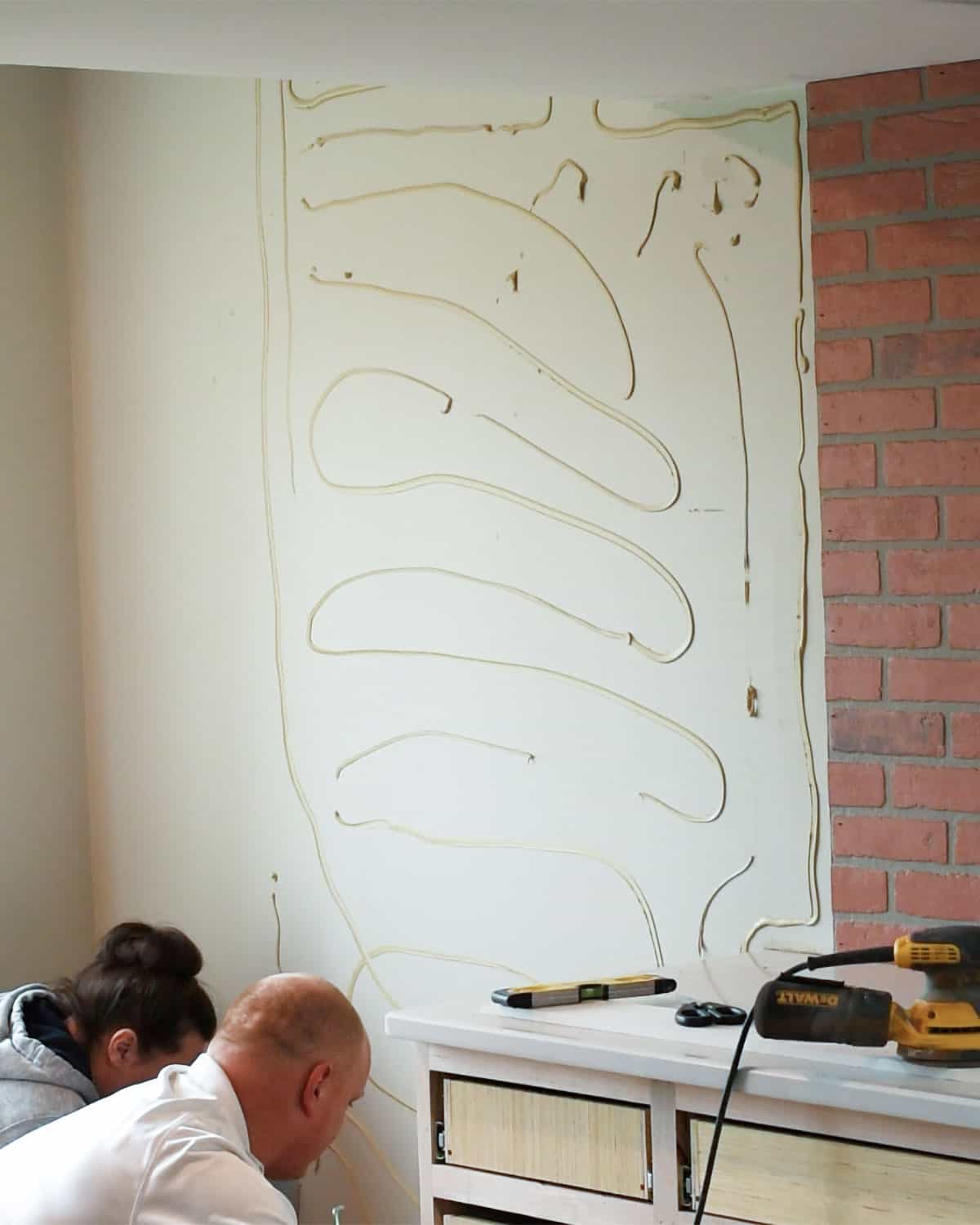 Man and woman with construction adhesive on the wall to add decorative panels.