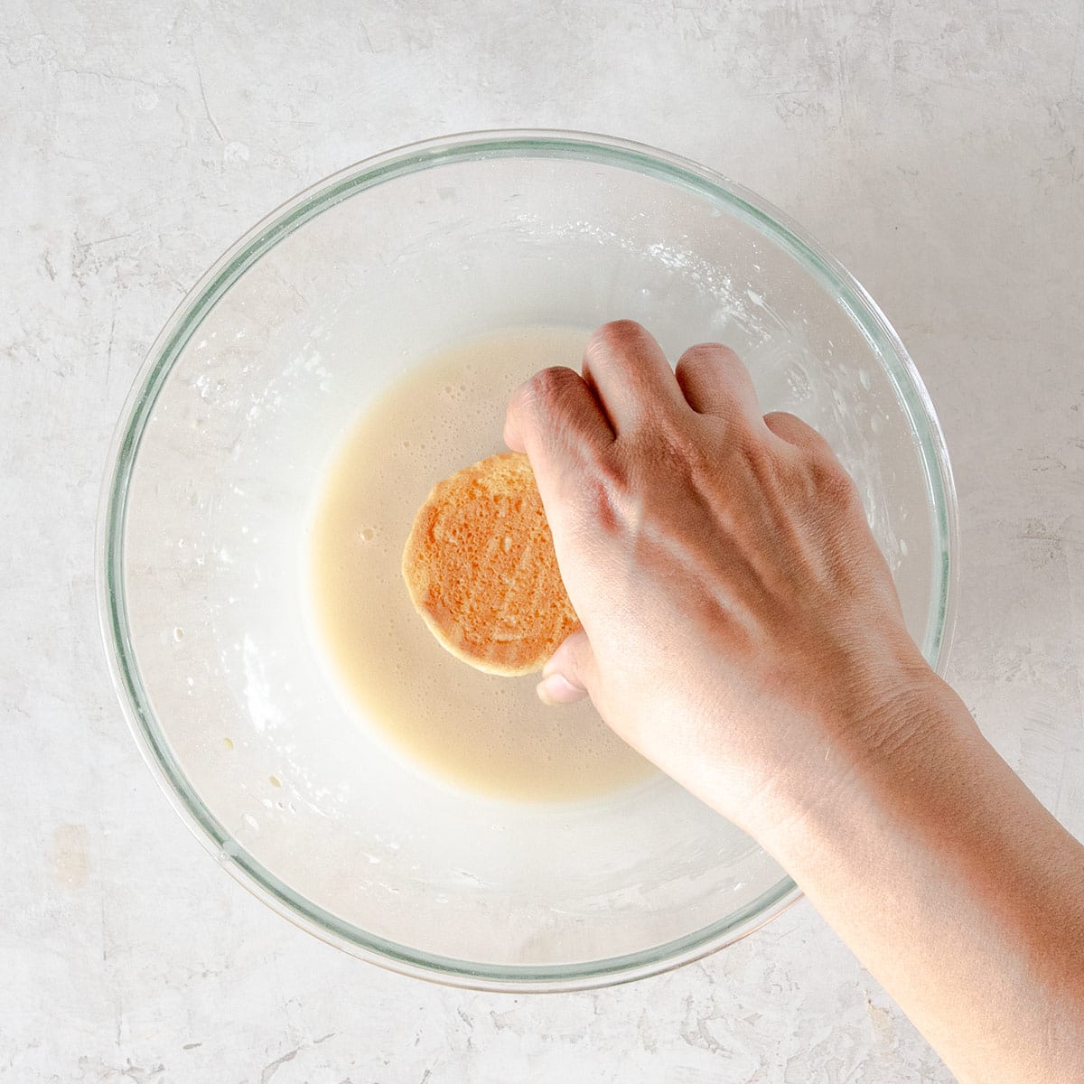 A woman dipping a cookie in icing to glaze it.