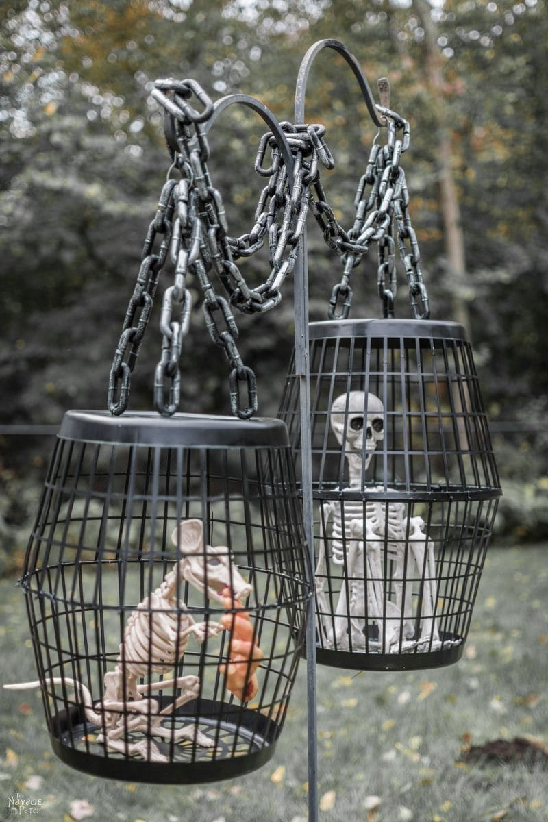 Hanging Halloween cage props are a simple DIY decoration made of black painted laundry hampers suspended from a shepherd's hook with skeleton prisoners.