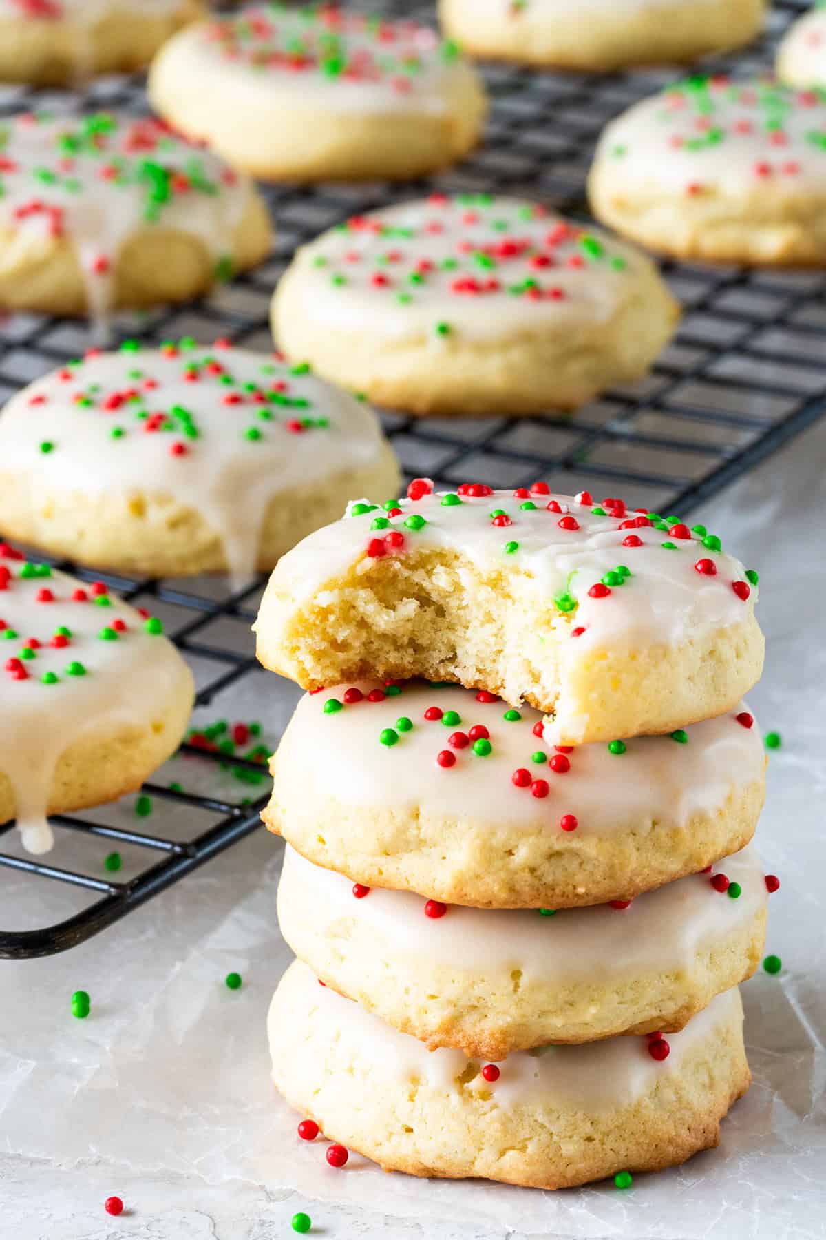 A stack of sour cream glazed cookies with sprinkles in front of a sheet of glazed cookies.