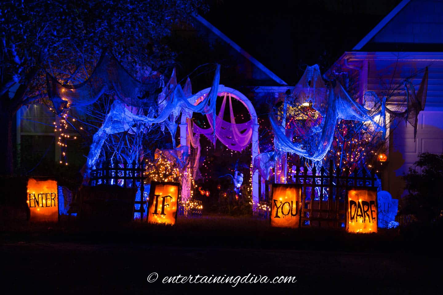 Outdoor Halloween scene features signs, archways, floodlights, string lights, and solar torches.