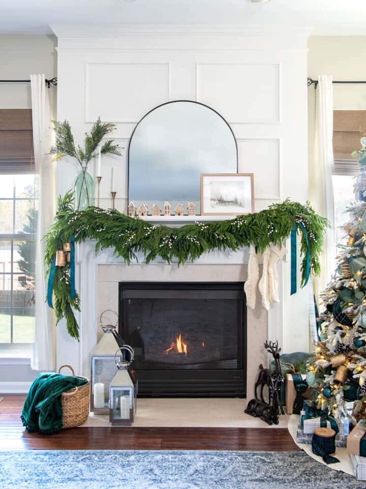 A fireplace mantel decorated for Christmas with garland, mirror, greenery, and candles.