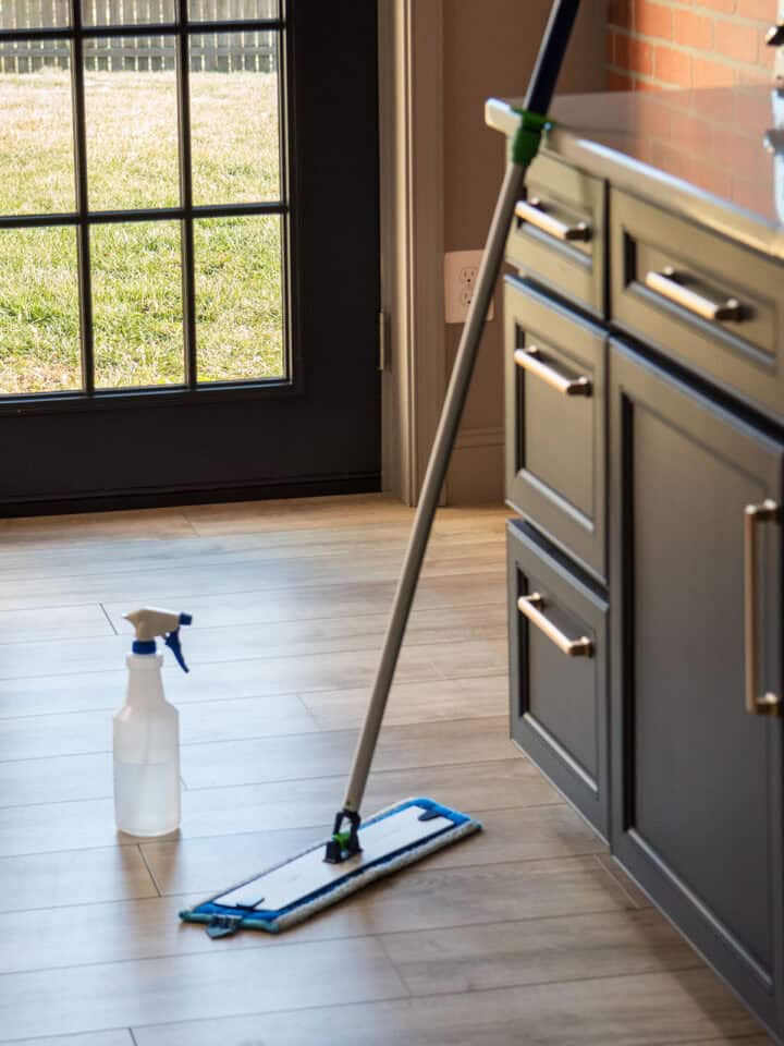 A mop leaning against black cabinets on top of a vinyl plank floor.
