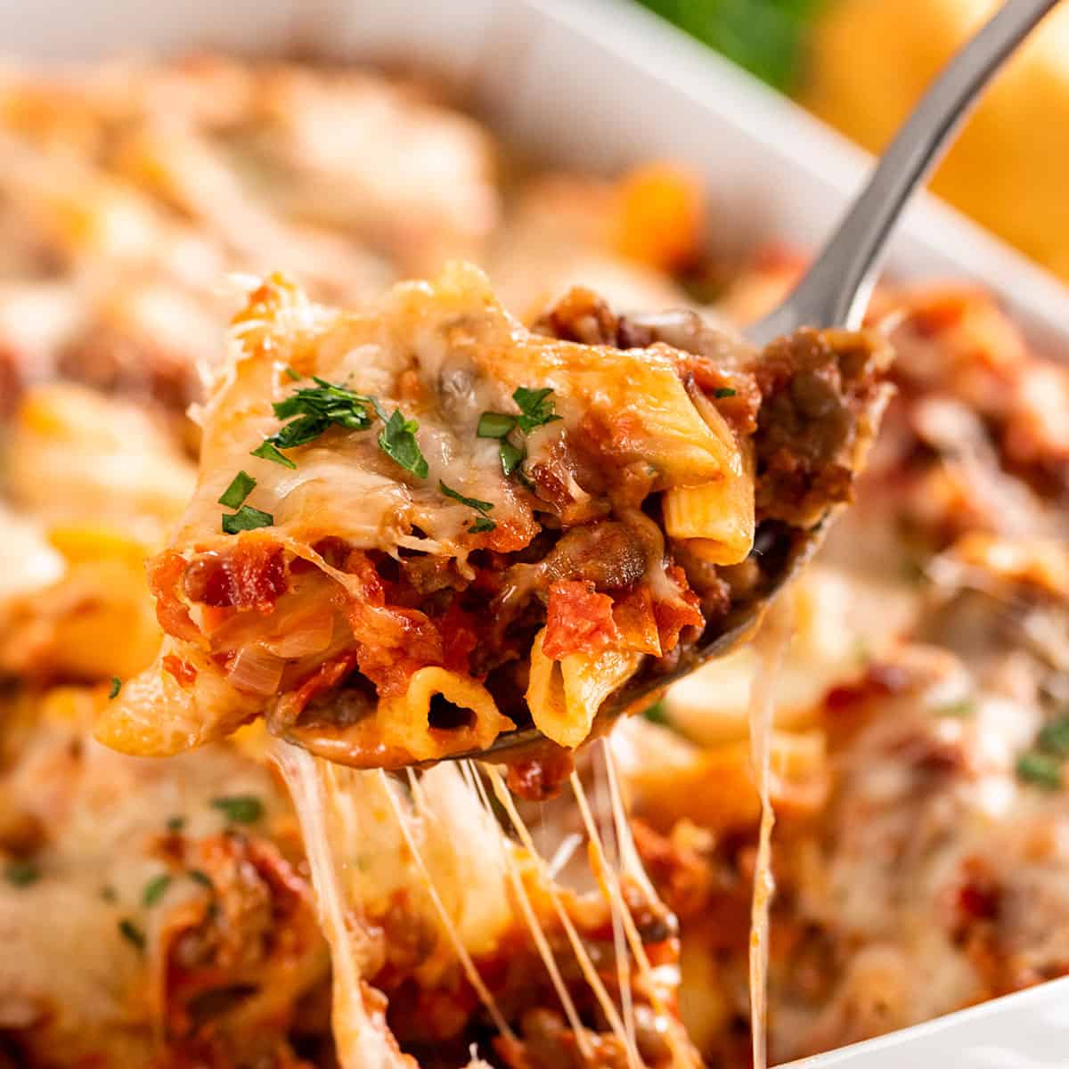 A serving spoon with bacon and sausage pasta bake shown for texture.