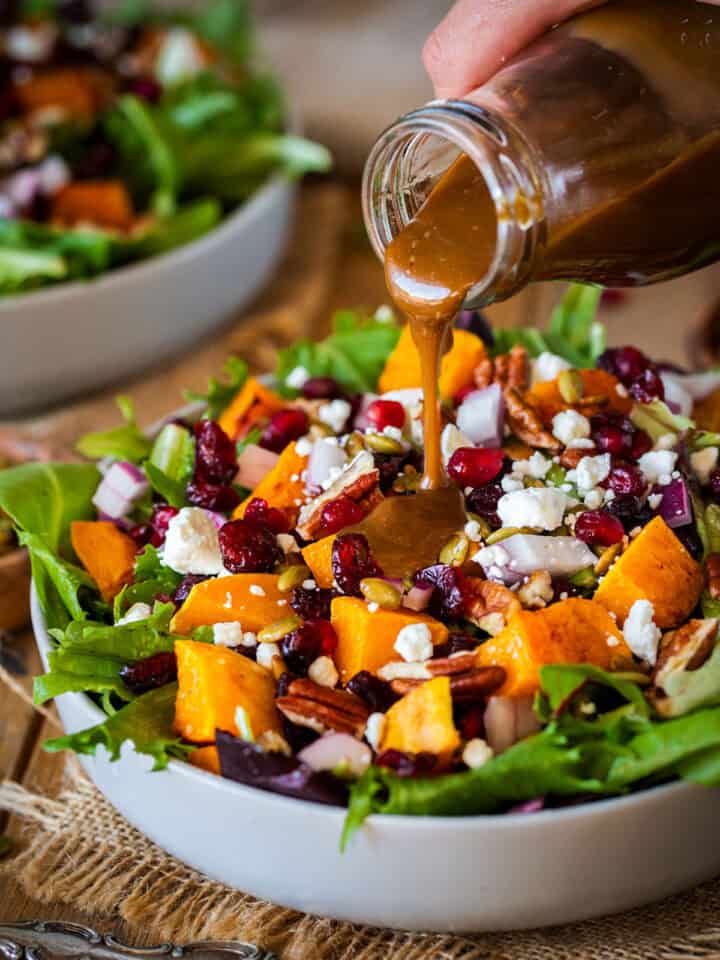 A bottle of balsamic vinaigrette being poured over a salad of squash and winter fruits.