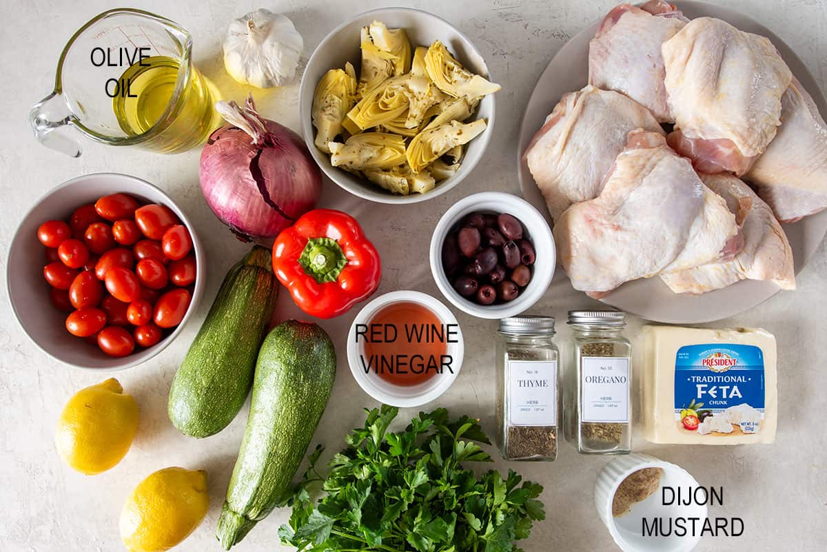 Ingredients to make roasted Mediterranean chicken with thighs, artichokes, vegetables, and dressing ingredients laid out on a table.