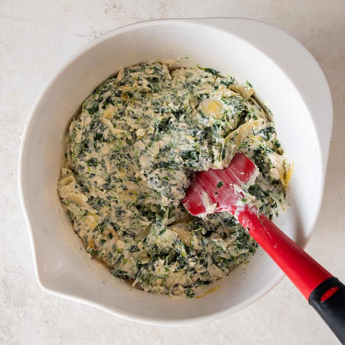 A bowl of spinach dip being stirred.