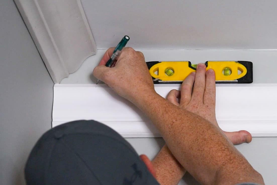 Man marking a second piece of board to cope to fit in the corner of the wall.