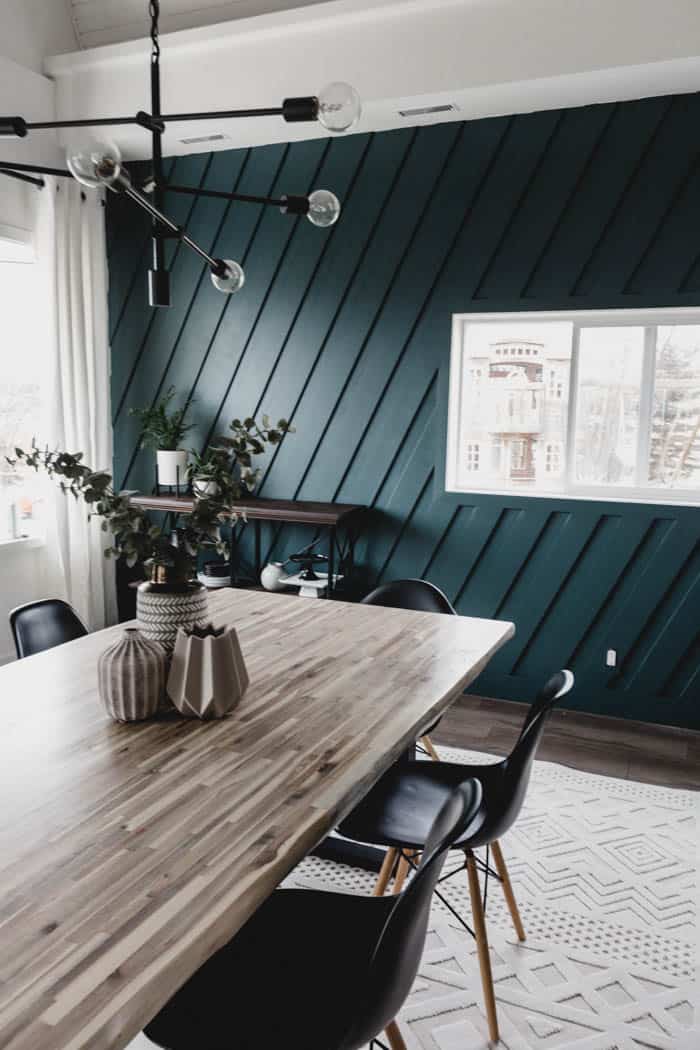 Forest green dining room with long table and diagonal slat walls.