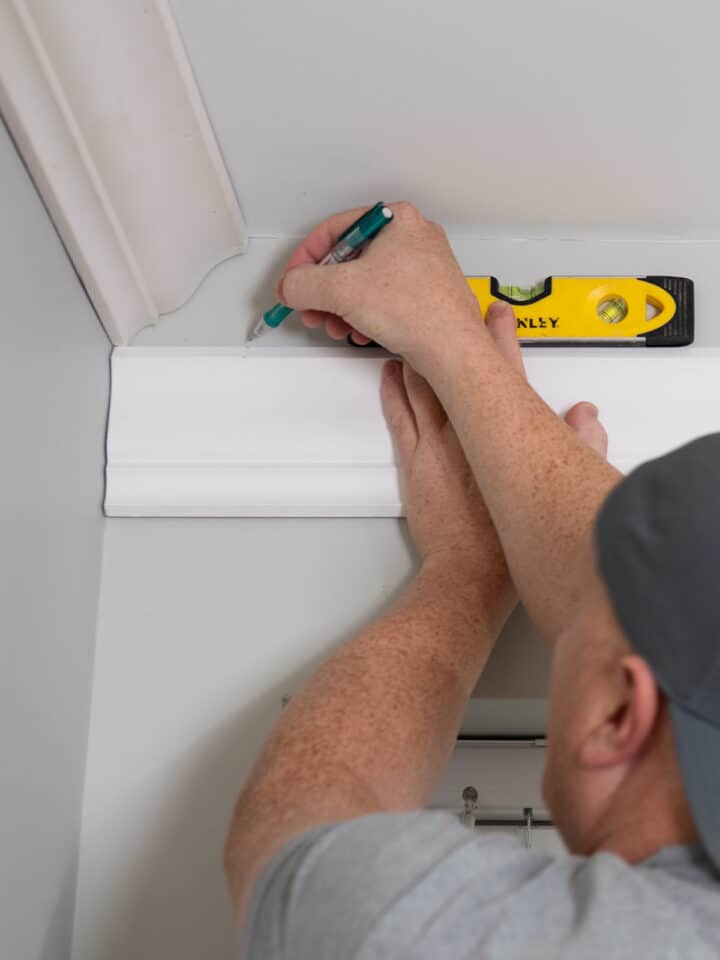 Man holding up crown molding to mark for installation.