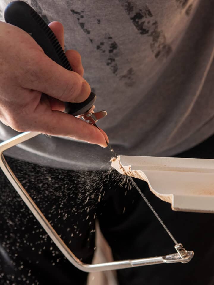 Man using a coping saw to cut crown molding for inside corner.
