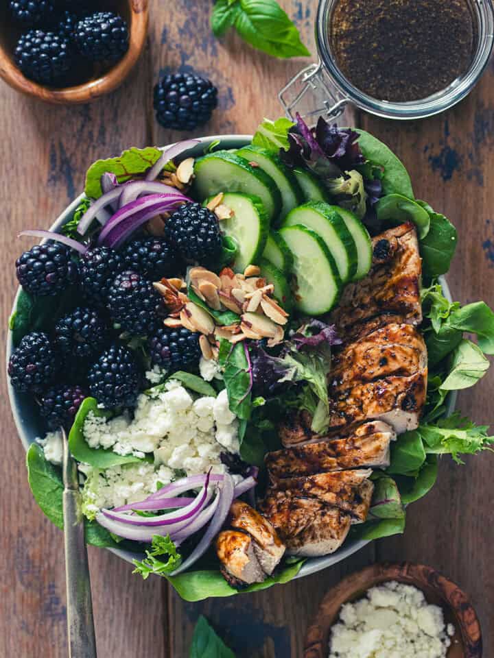 Top down flat lay of blackberry chicken salad with balsamic dressing and basil in the background.