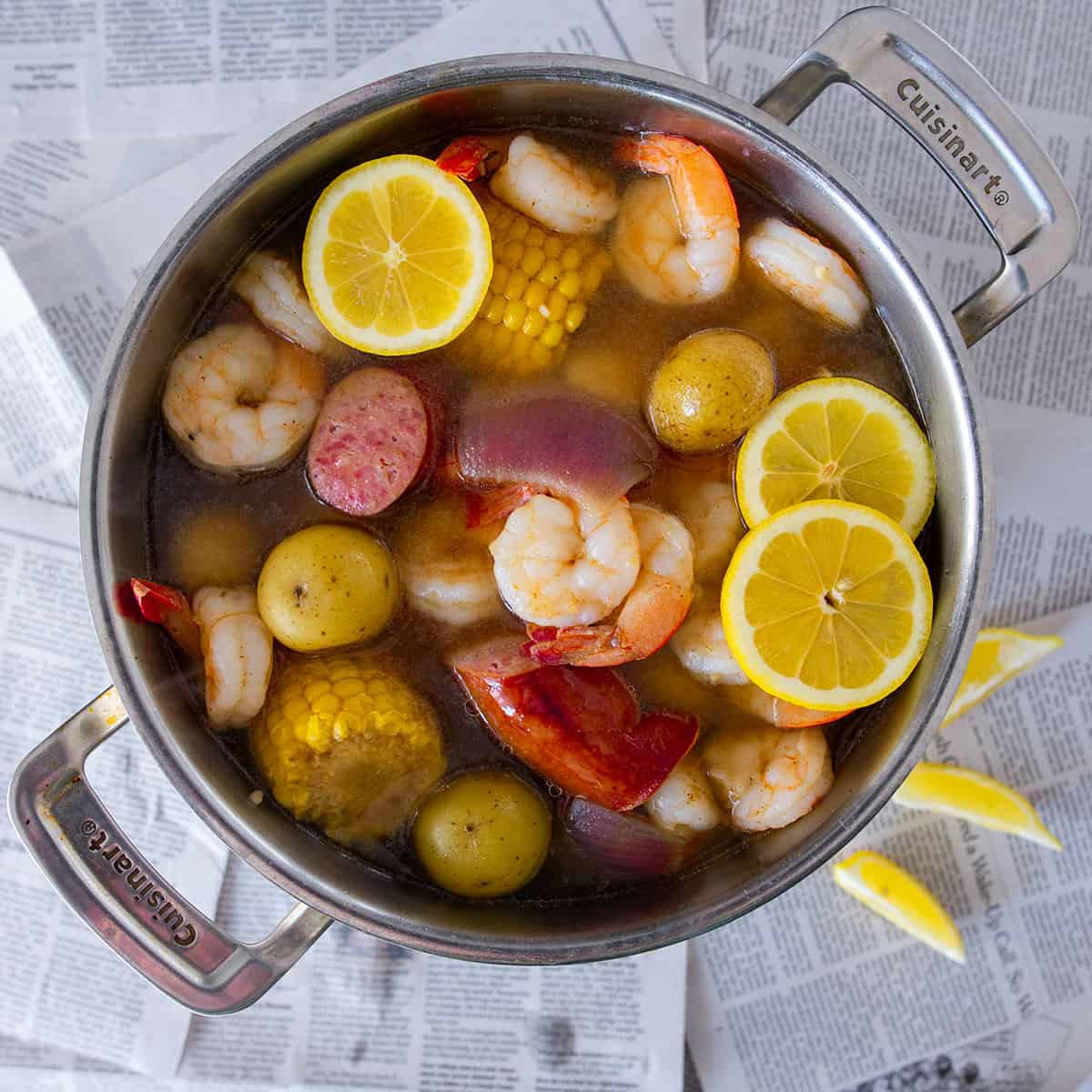 Top down look into a pot of Cajun shrimp boil with potatoes, corn, onions, lemons, and sausage.