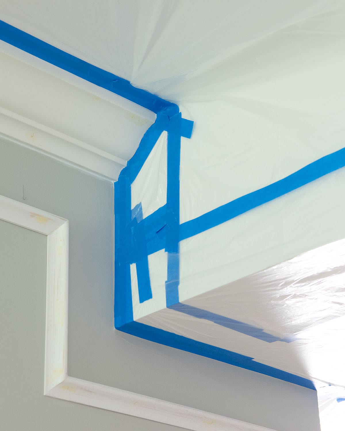 The corner of a ceiling with crown molding and a soffit covered with plastic to show how to mask tricky areas.