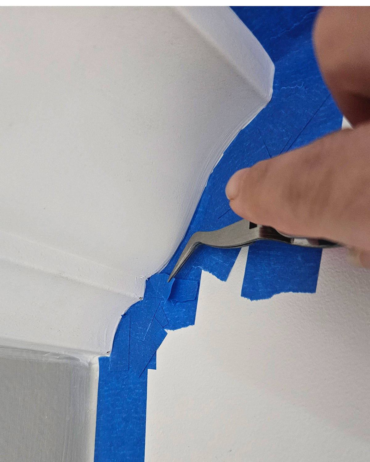 A hand using tweezers to place a tiny bit off tape into a corner.