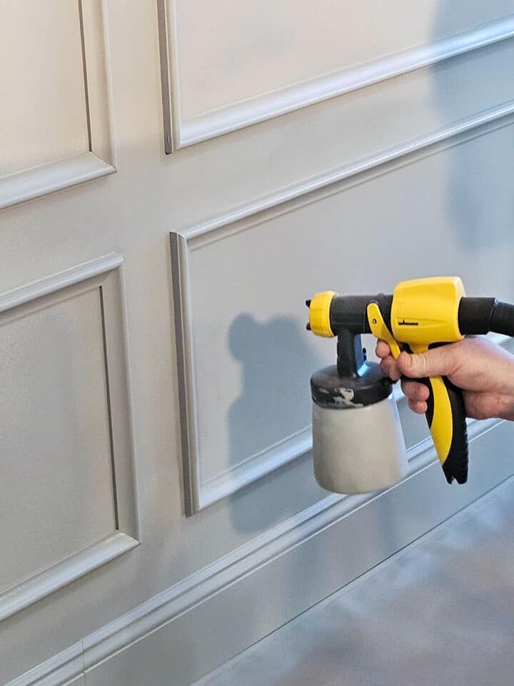 Close up of a man spraying a gray wall with a spray gun.