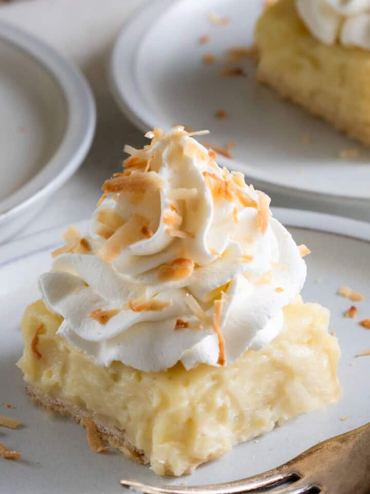A slice of coconut cream pie bars on a plate with toasted coconut on top.