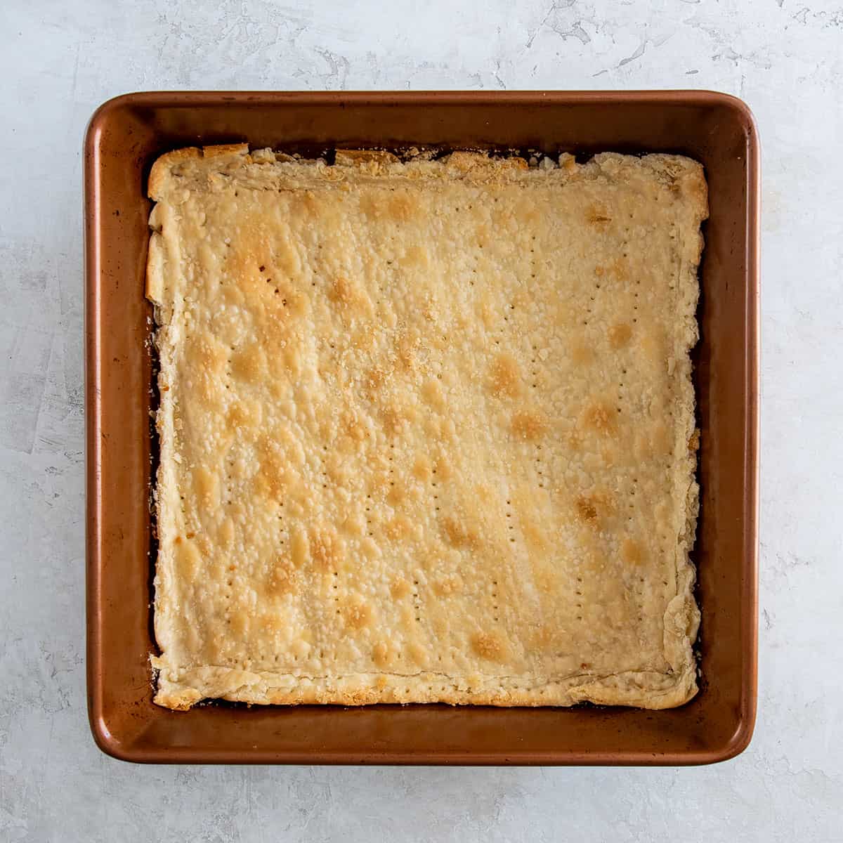 A baked and trimmed pie crust in a square baking dish.