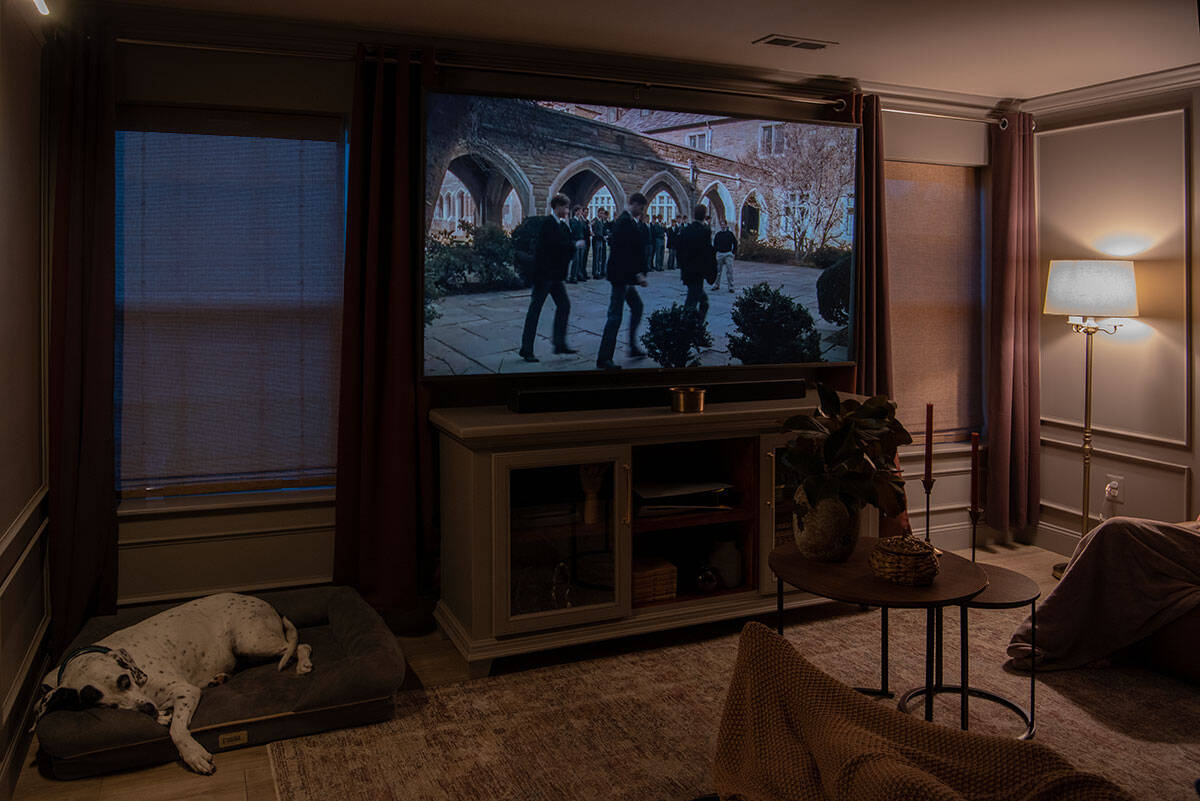 A movie theatre room showing a family enjoying a movie with a dog, blankets, and cozy lighting.