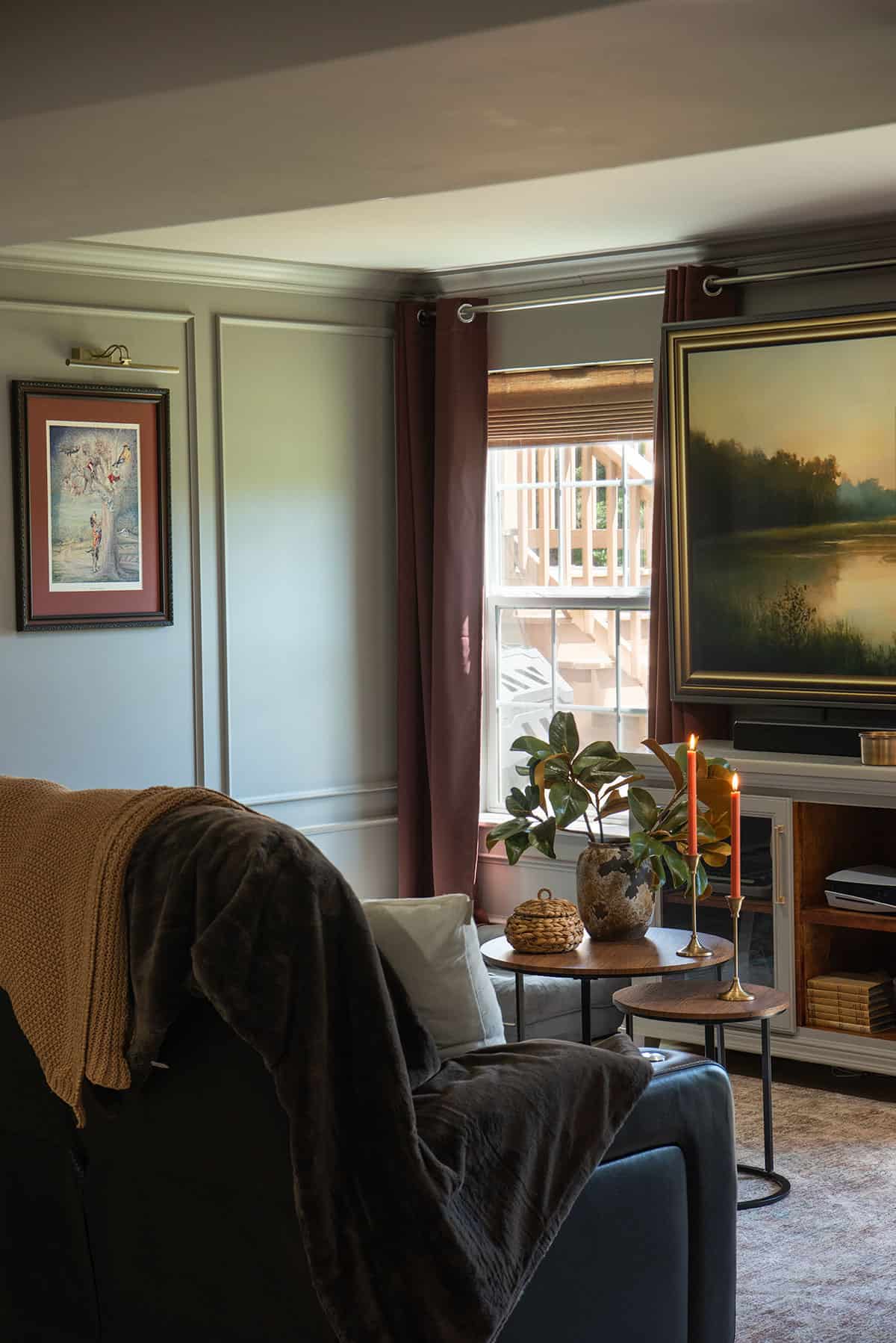 A moody traditional living room with a large painting on the wall and windows.